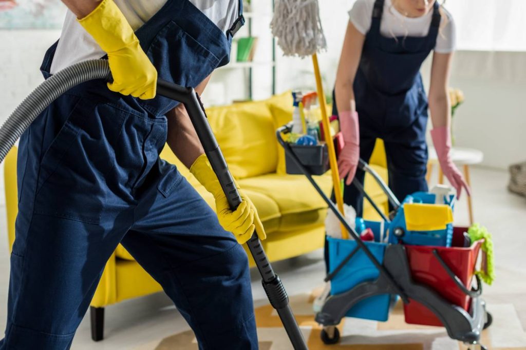 cropped view of cleaners in overalls and rubber gloves cleaning apartment