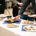 People in suits serve themselves at the buffet and eat delicious food at a business event. There are snacks and finger food.