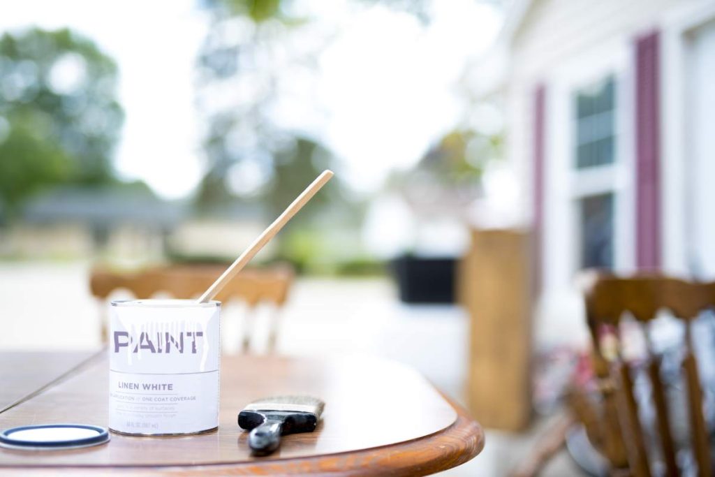 A closeup shot of a can of pain near a paintbrush on a wooden table with a blurred background