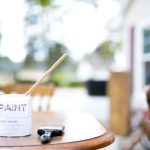 A closeup shot of a can of pain near a paintbrush on a wooden table with a blurred background