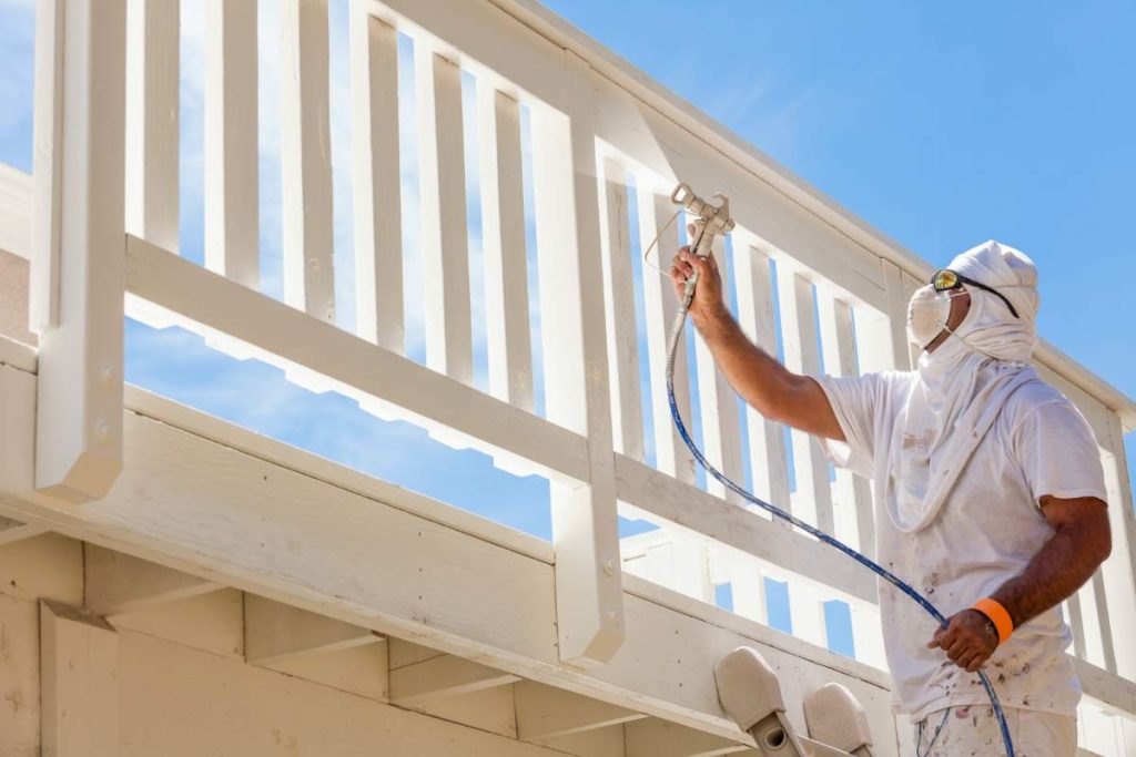 House Painter Wearing Facial Protection Spray Painting A Deck of A Home.